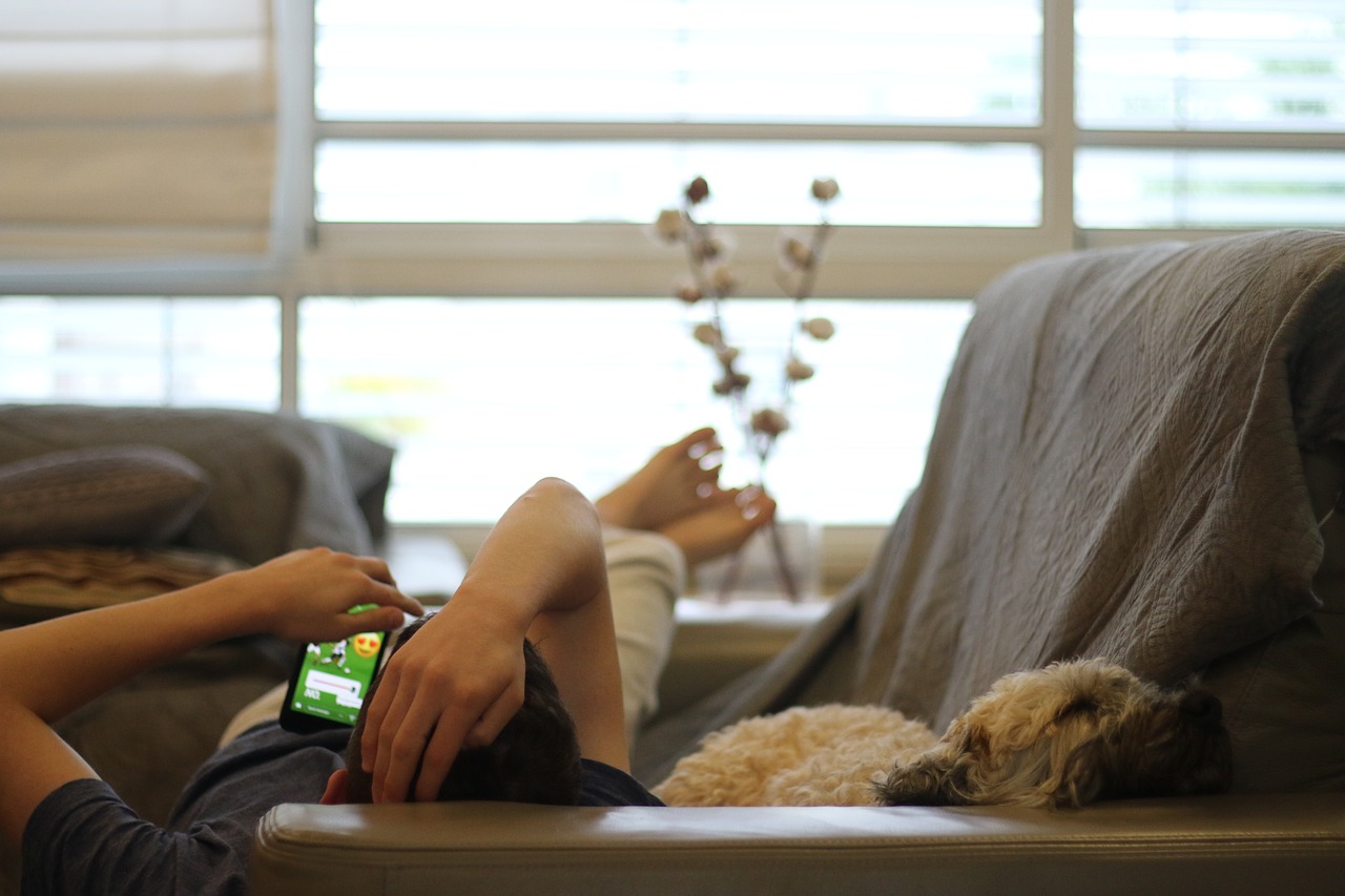 Mann liegt mit Smartphone auf dem Sofa, sein Hund liegt neben ihm