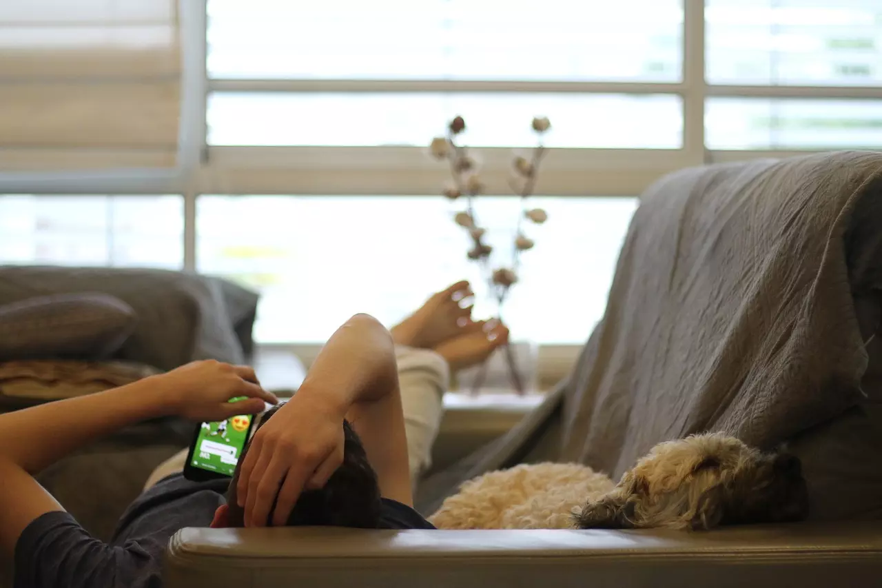 Mann liegt mit Smartphone auf dem Sofa, sein Hund liegt neben ihm