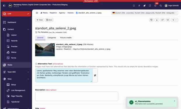 TYPO3 v14 Backen: Ergebnisse eines ai_filemetadata Laufes: Ein leerer, gepflasterter Weg zwischen zwei roten Backsteingebäuden mit vielen großen, rechteckigen Fenstern und einer geöffneten Torstruktur am Ende, umgeben von beidseitig gepflanzten jungen Bäumchen auf einer kleinen Grünfläche.